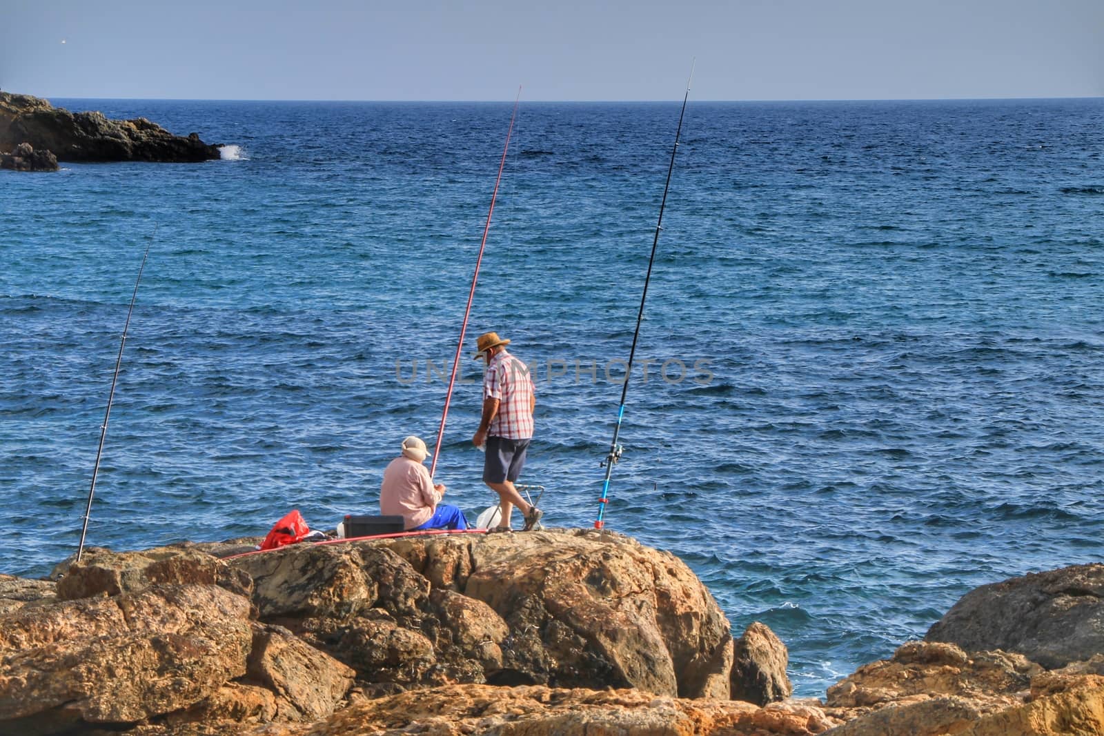 Isla Plana, Murcia, Spain- October 2, 2019: Fisherman and his wife fishing on the rocks in the evening on Isla Plana beach in a sunny day. Cartagena province, Murcia,Spain.