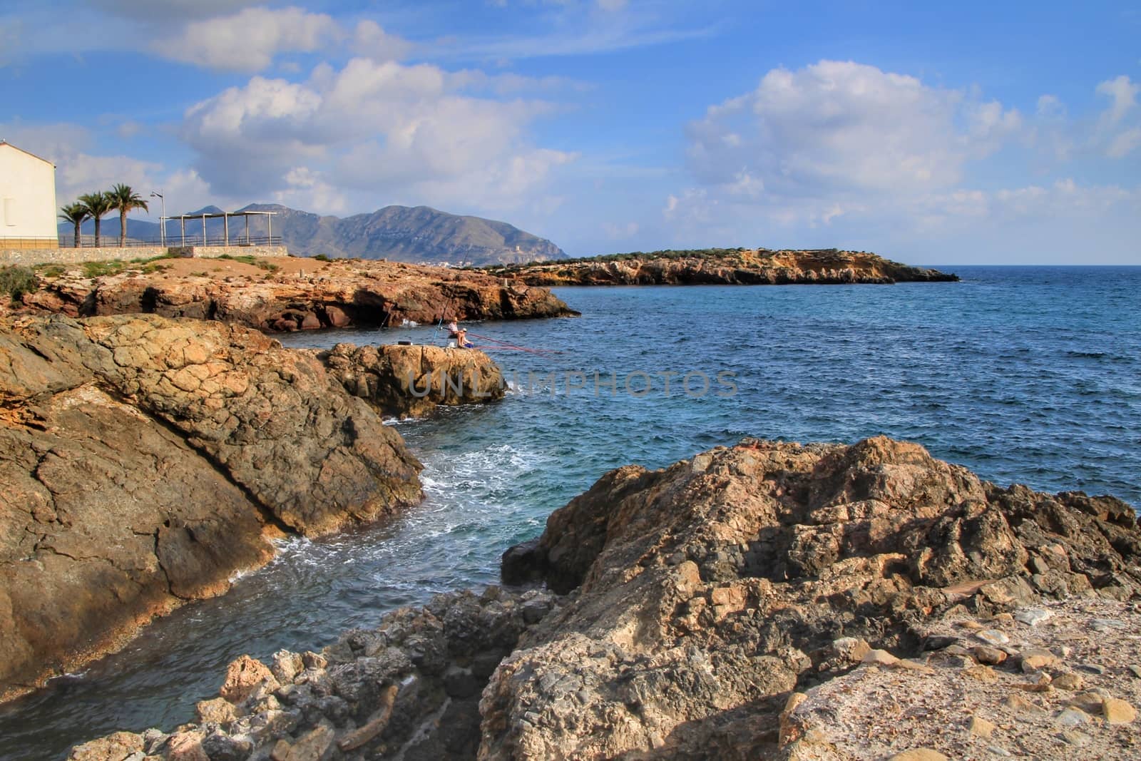 Isla Plana, Murcia, Spain- October 2, 2019: Fisherman and his wife fishing on the rocks in the evening on Isla Plana beach in a sunny day. Cartagena province, Murcia,Spain.