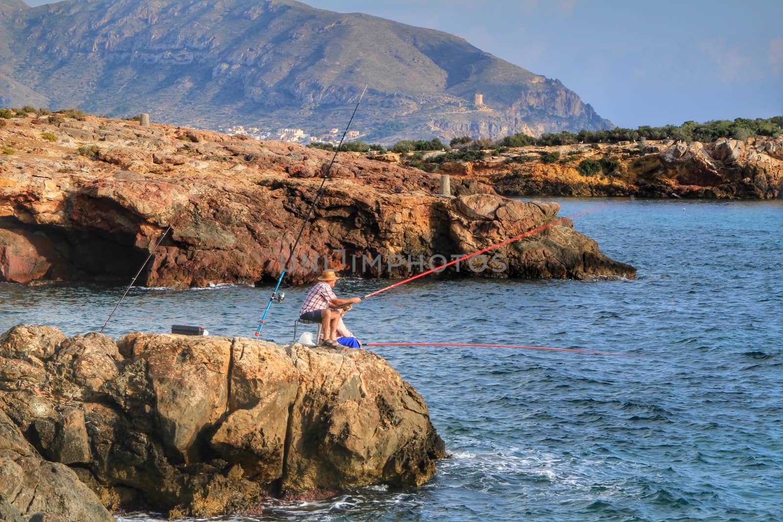 Isla Plana, Murcia, Spain- October 2, 2019: Fisherman and his wife fishing on the rocks in the evening on Isla Plana beach in a sunny day. Cartagena province, Murcia,Spain.