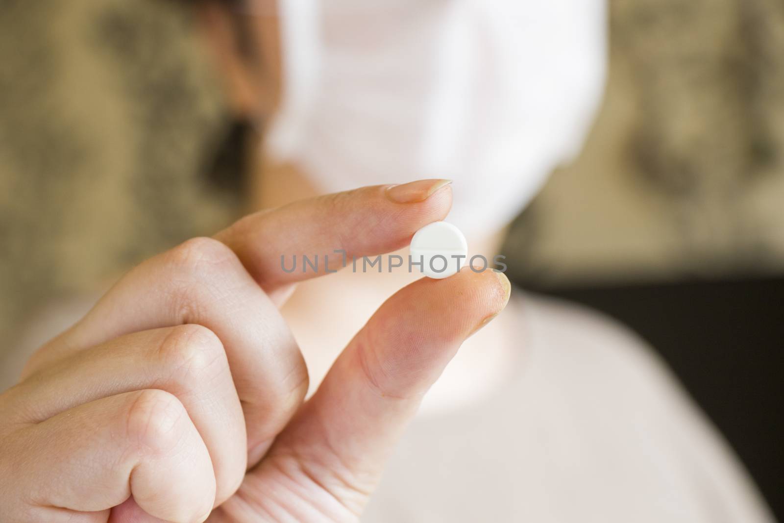 Drugs and pills, medicine and healthy care. Woman holding white pill in hand on the blur face background.