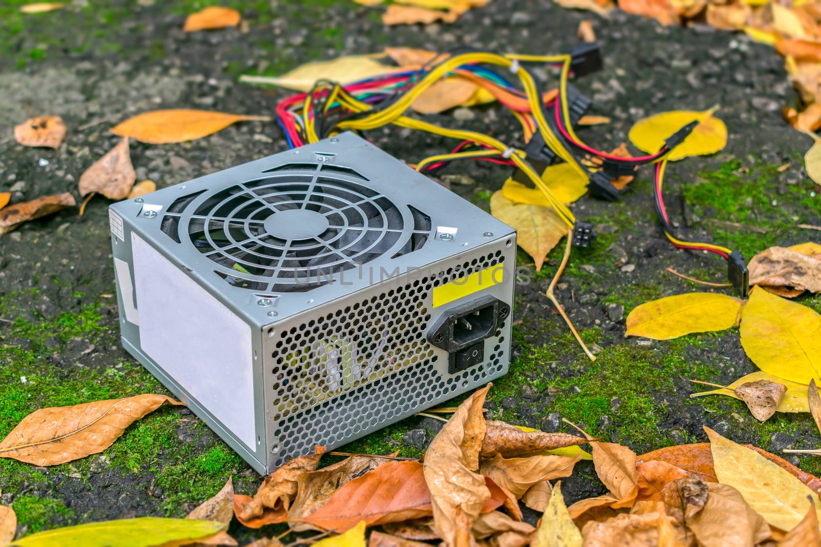 An old computer power supply discarded in a landfill lies in the autumn foliage