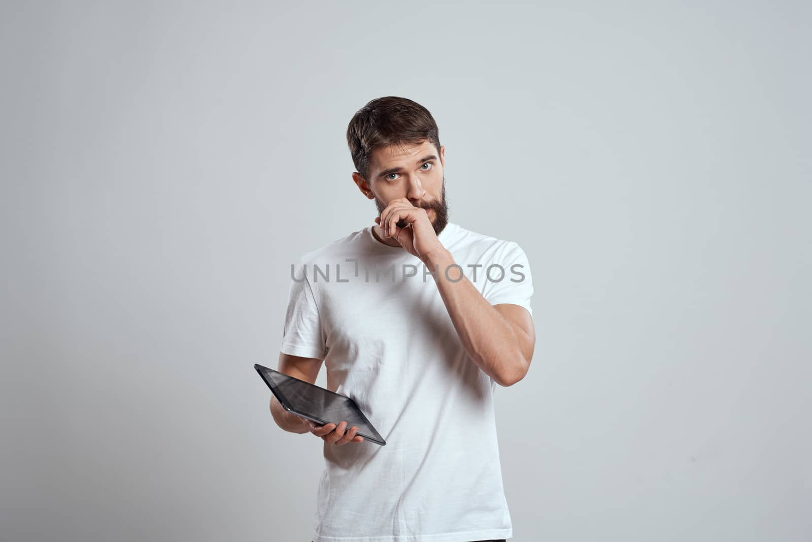 A man in a white T-shirt with a tablet in his hands emotions technology light background. High quality photo