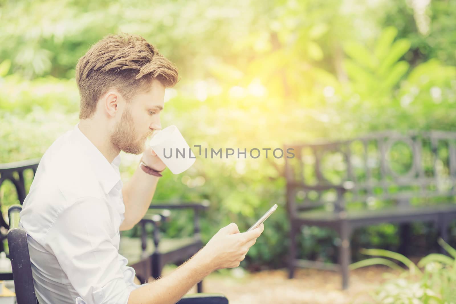 Business young handsome man drink cup of coffee using mobile phone sitting in the park, communication concept.
