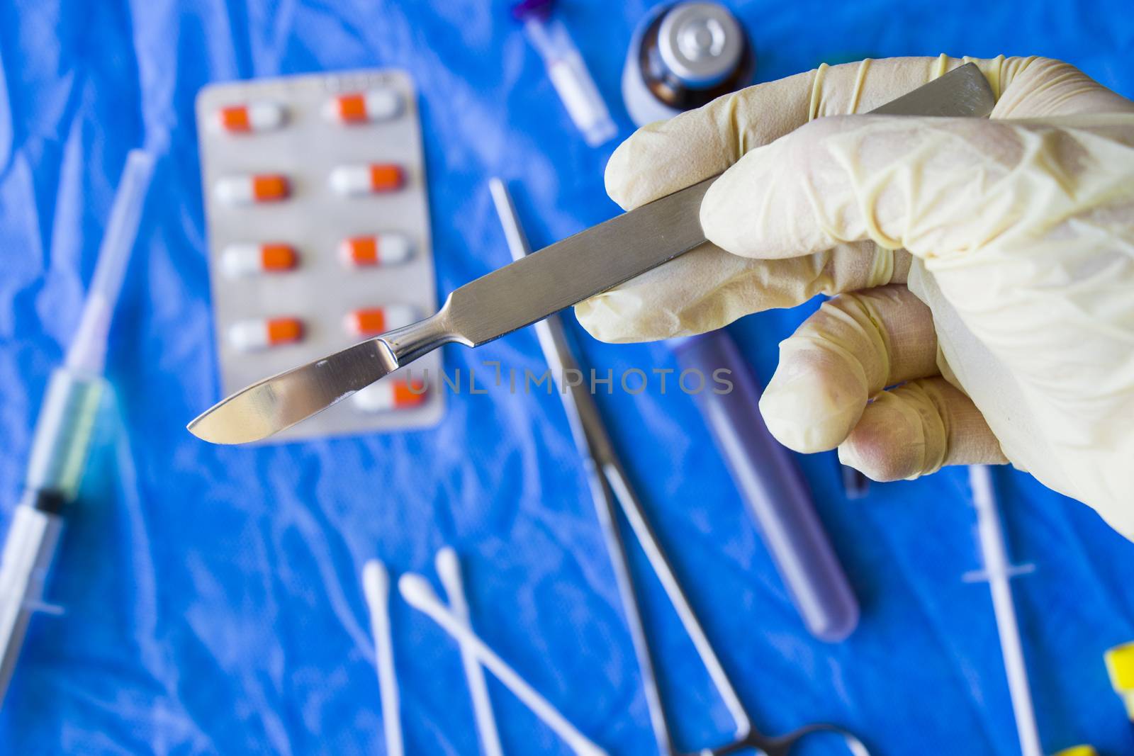 Hand with glove holding surgery blade, drugs, ampule,needle and blood tube on the background