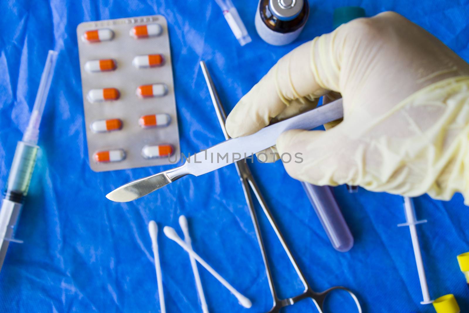 Hand with glove holding surgery blade, drugs, ampule,needle and blood tube on the background