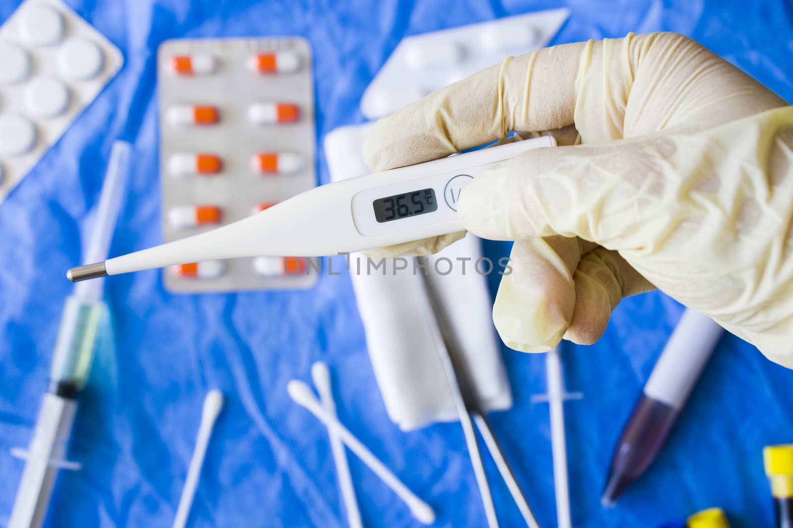 Body thermometer holding in hand, glove and doctors hand, drugs on the background