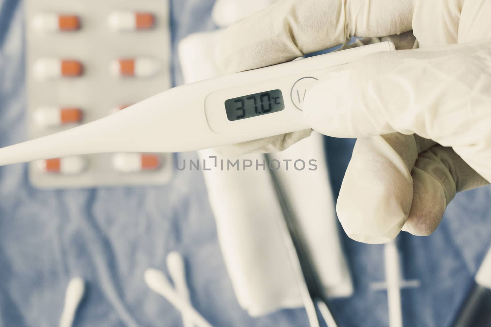Body thermometer holding in hand, drugs on the background by Taidundua