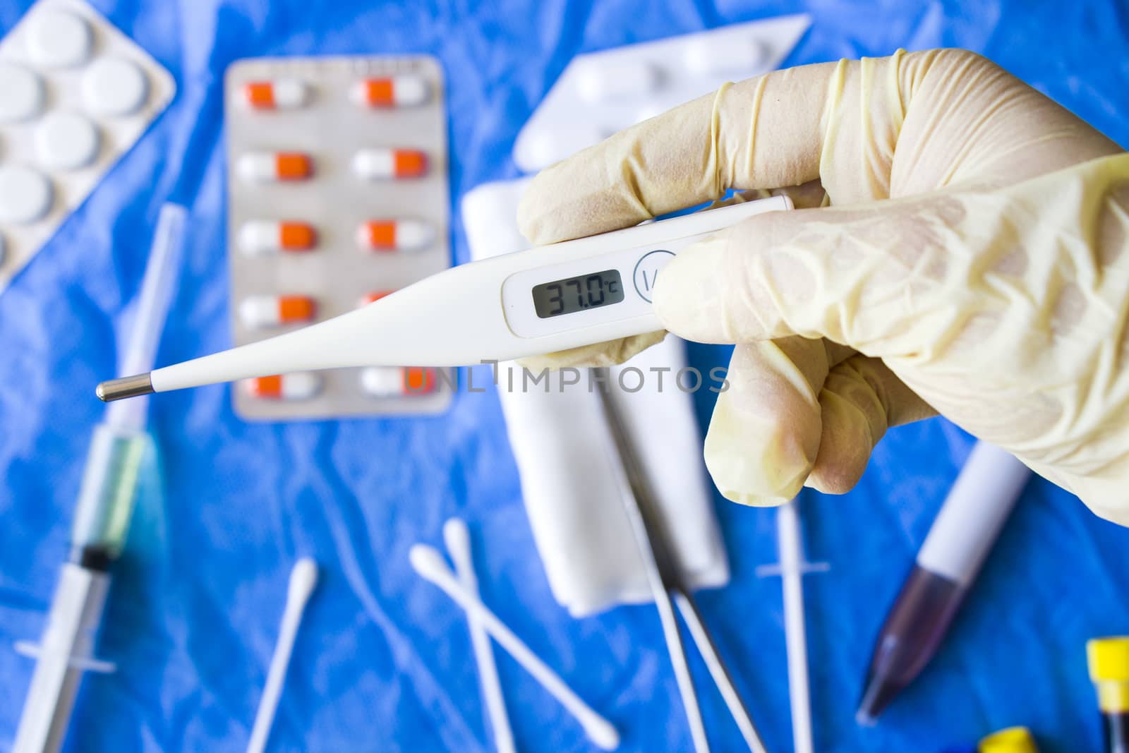 Body thermometer holding in hand, glove and doctors hand, drugs on the background