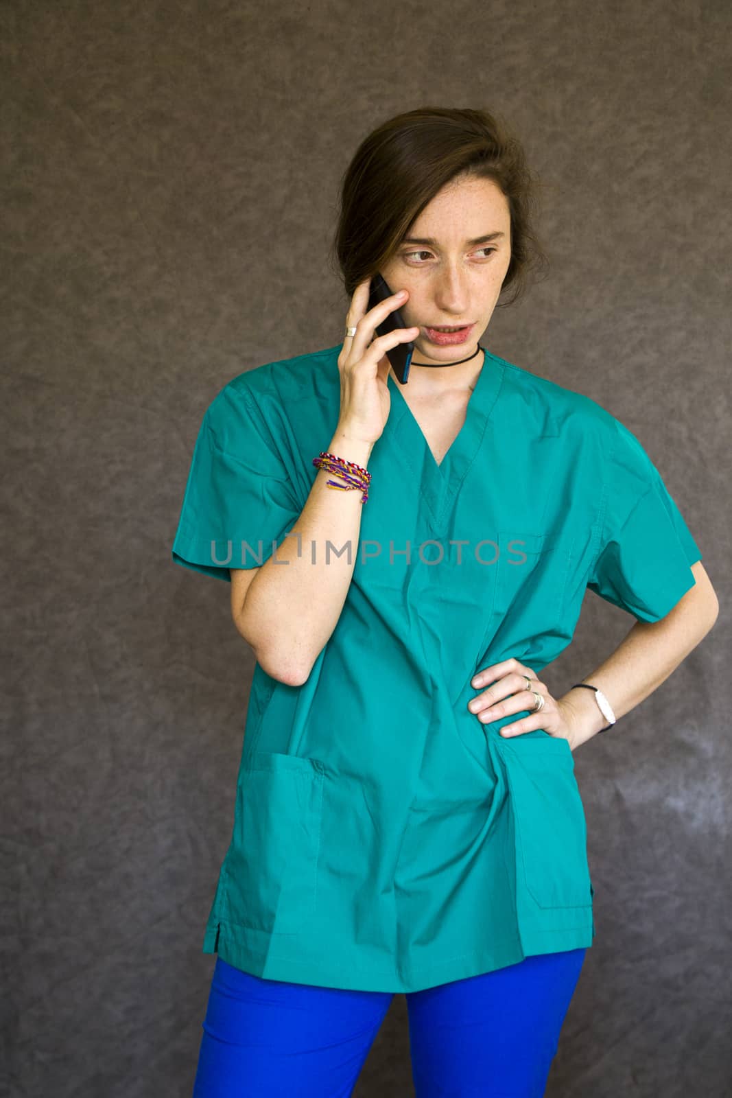 Woman portrait in medical nurse and doctors uniform on the gray background, woman talking on the mobile phone