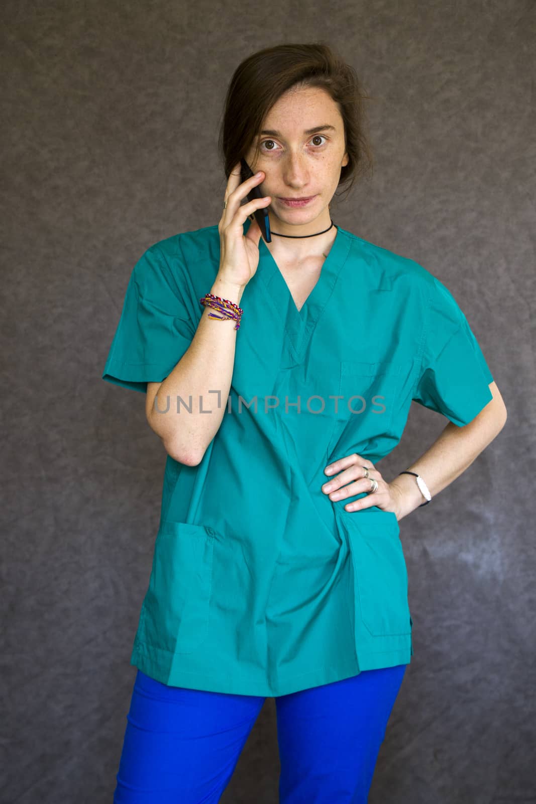 Woman portrait in medical nurse and doctors uniform on the gray background, woman talking on the mobile phone