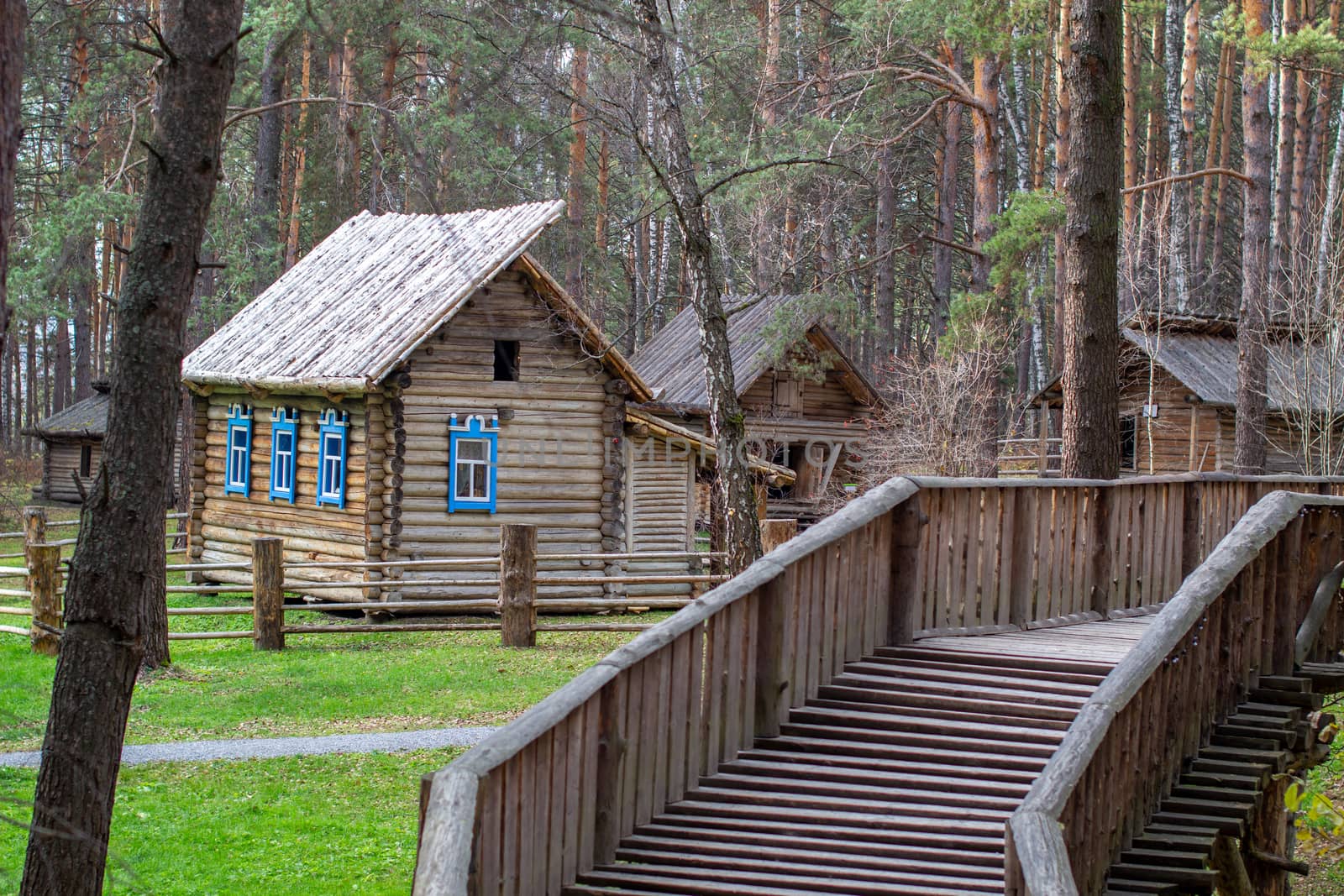 Wooden house with a manor house in the forest. The house has painted Windows. A wooden bridge leads to the house across the river. 