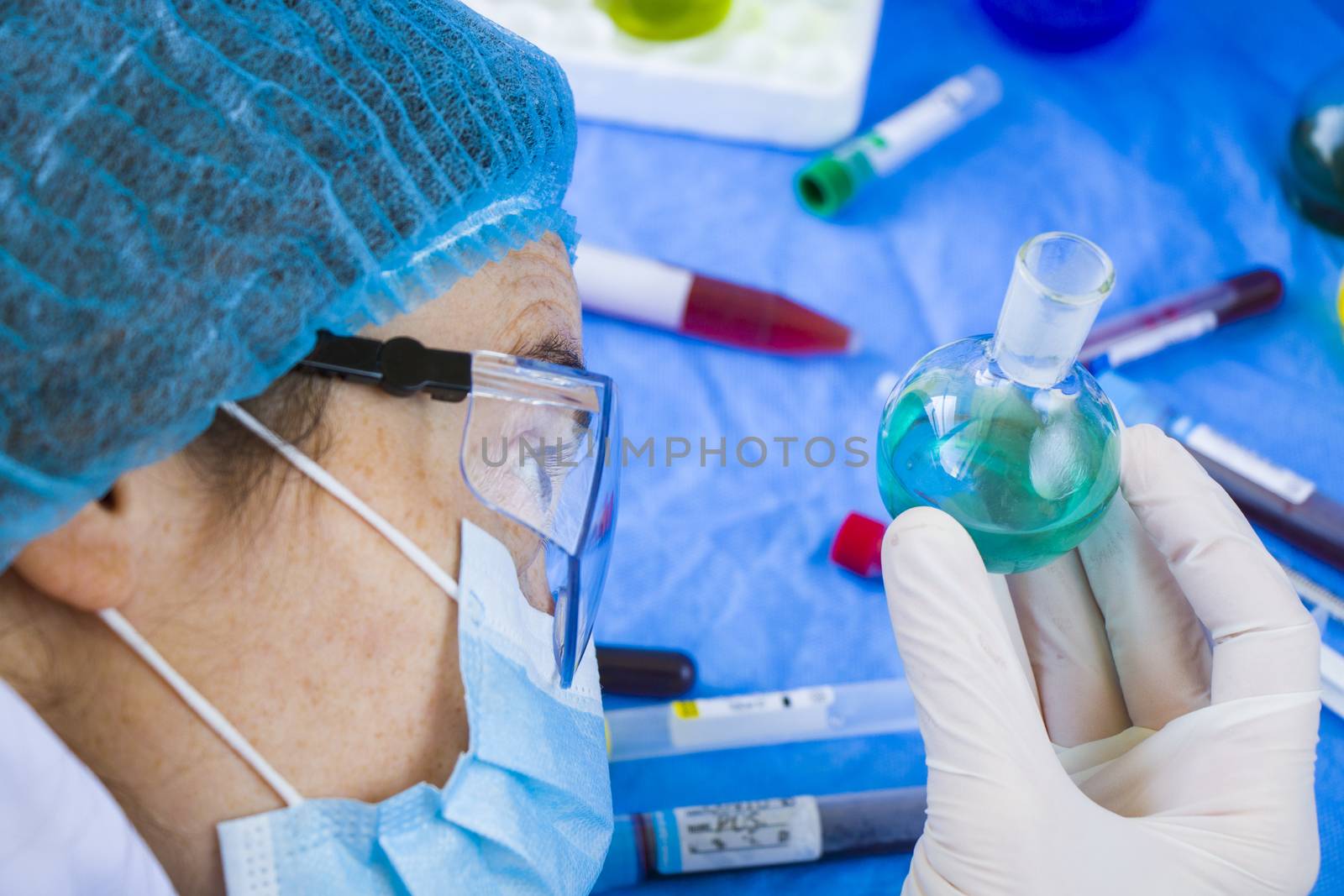 Doctors in uniform, face mask and glasses looking at sample in laboratory, colorful liquid chemical elements, research diagnoses