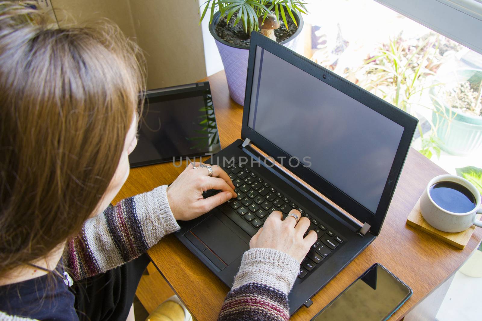 Woman working with notebook in workplace, digital tablet, mobile phone, coffee and plants by Taidundua