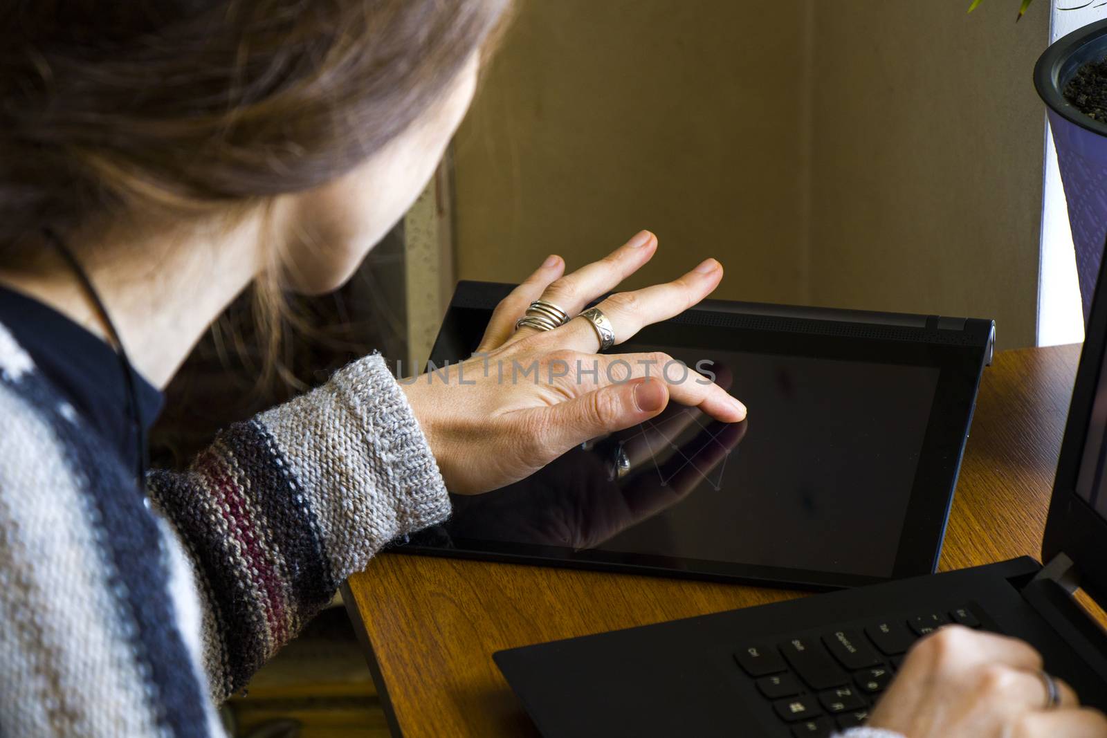 Woman working in office with digital tablet and notebook, writing and typing on the device