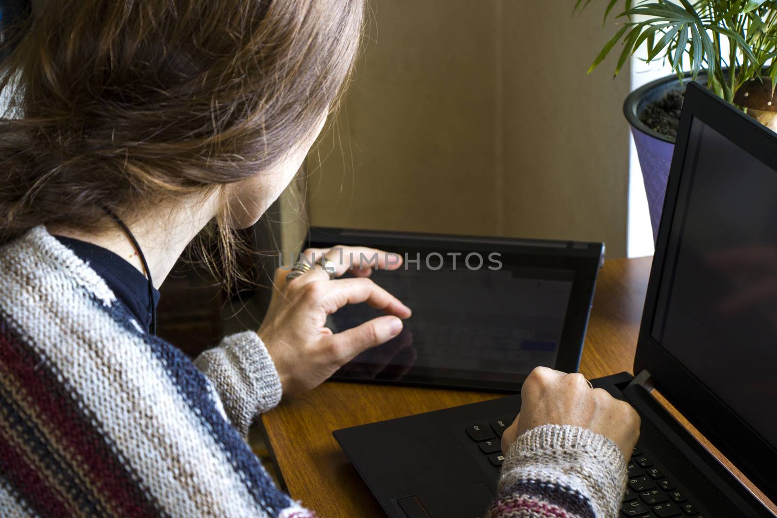 Woman working in office with digital tablet and notebook, writing and typing on the device