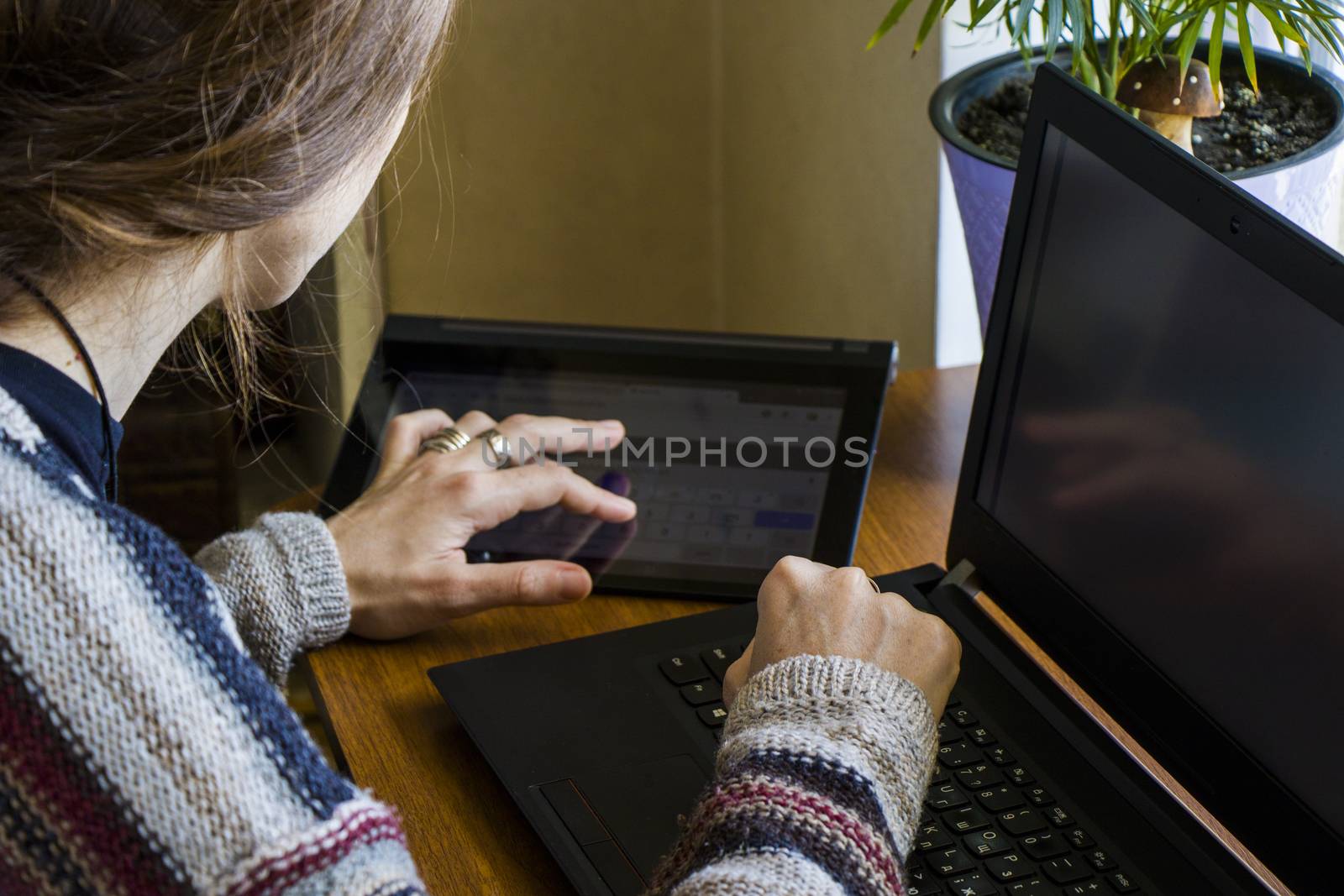 Woman working in office with digital tablet and notebook, writing and typing on the device