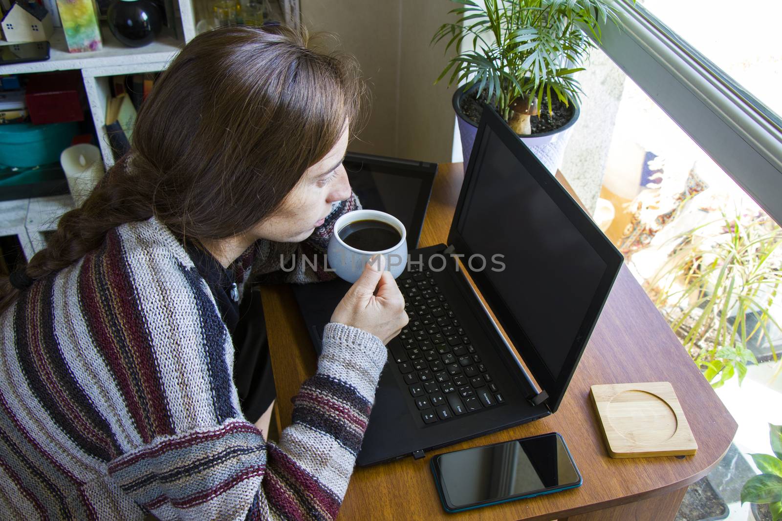 Woman working with notebook in workplace, digital tablet, mobile phone, coffee and plants by Taidundua