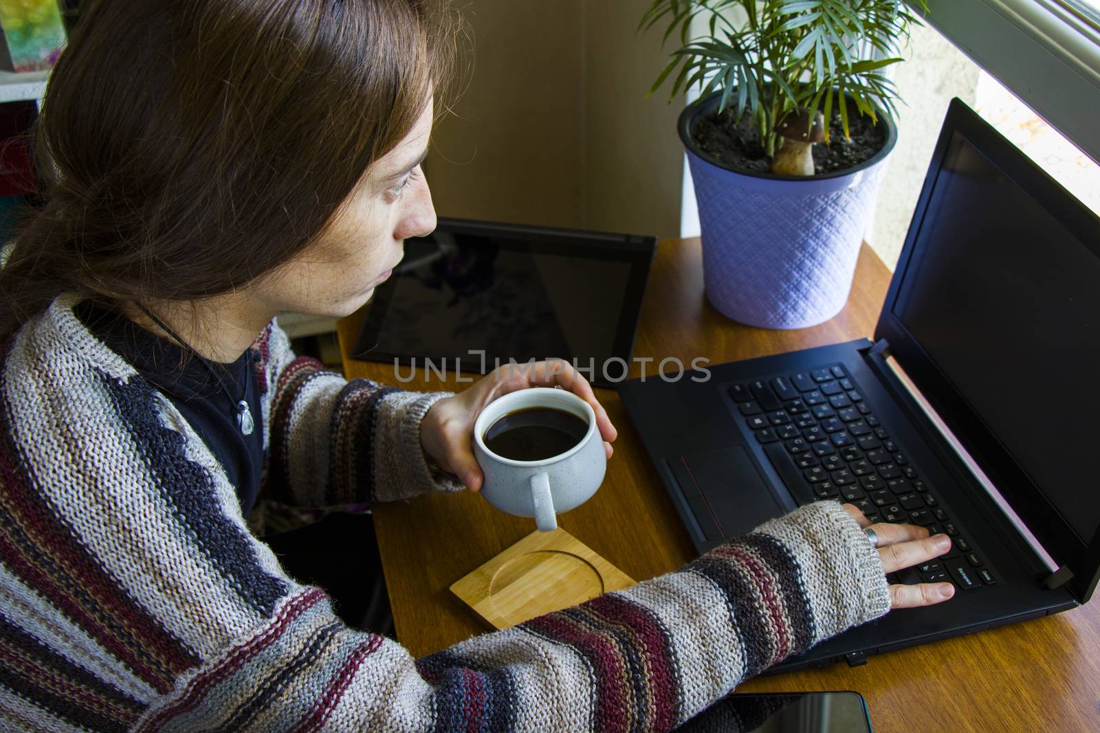 Woman working with notebook in workplace, digital tablet, mobile phone, coffee and plants by Taidundua