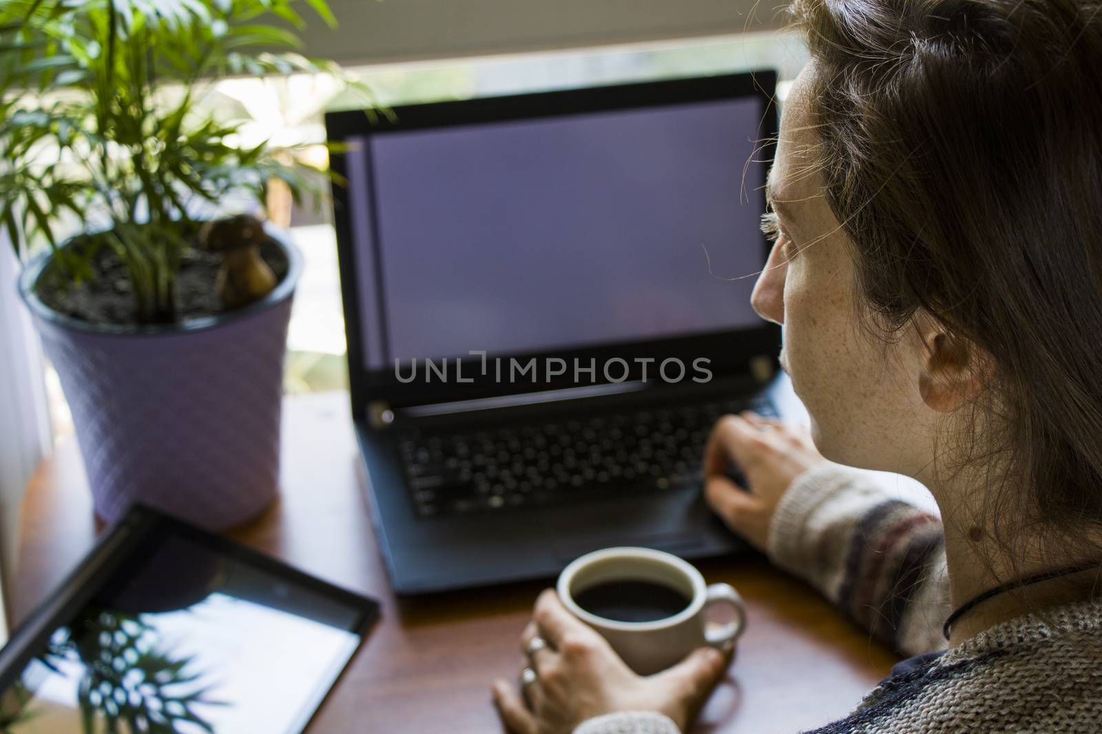 Woman working in office with digital tablet and notebook, writing and typing on the device