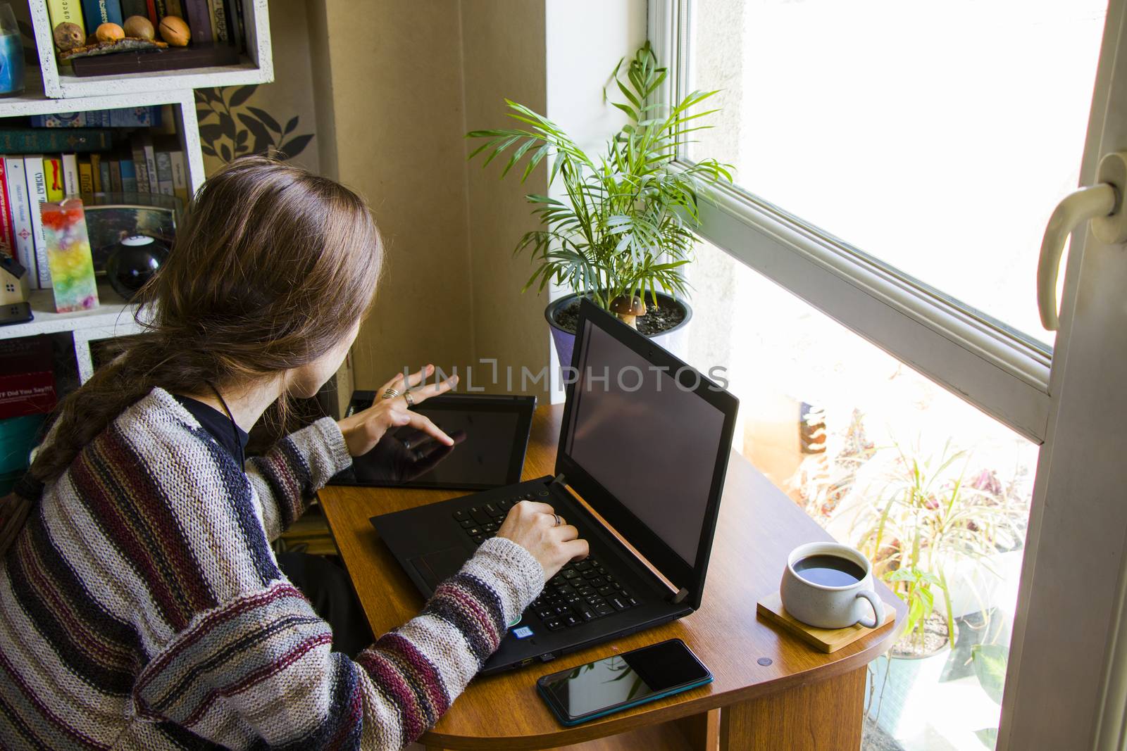 Woman working with notebook in workplace, digital tablet, mobile phone, coffee and plants by Taidundua