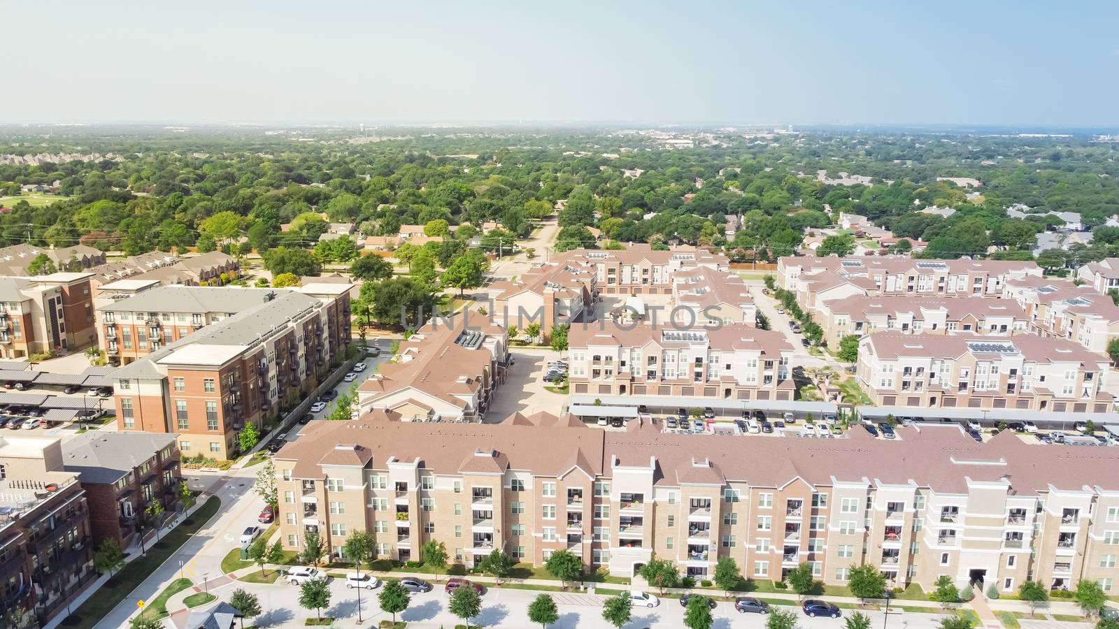 Flyover brand new multistory apartment complex with covered parking lots and suburban residential area in background. Master-planned community and census-designated sprawl in Flower Mound, TX