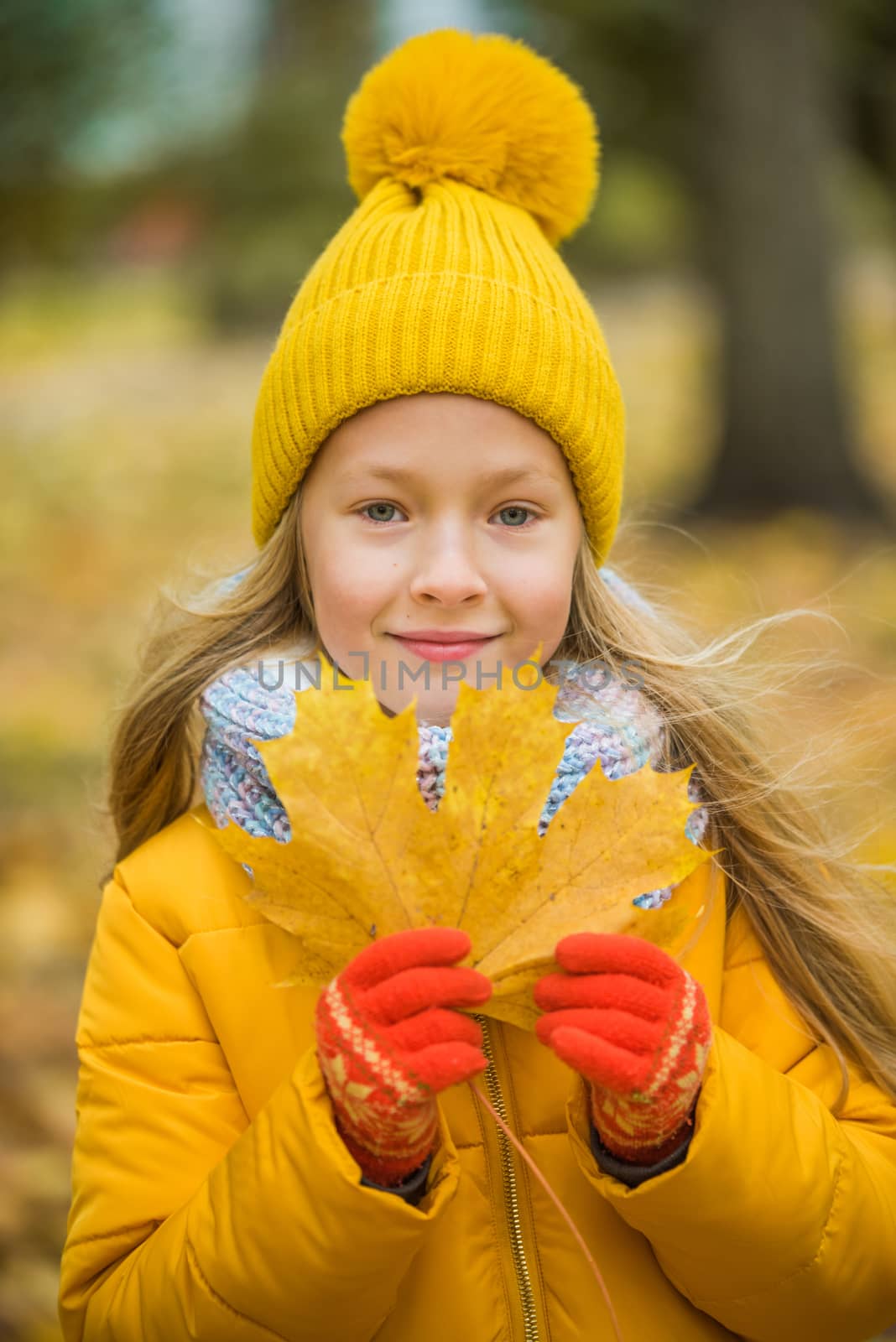Little girl with blond hair in autumn background in yellow clothing with yellow leaf