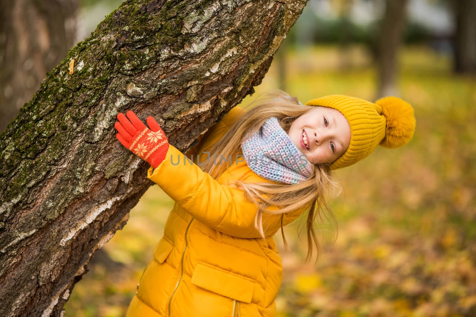 Little girl with blond hair in autumn background in yellow clothing