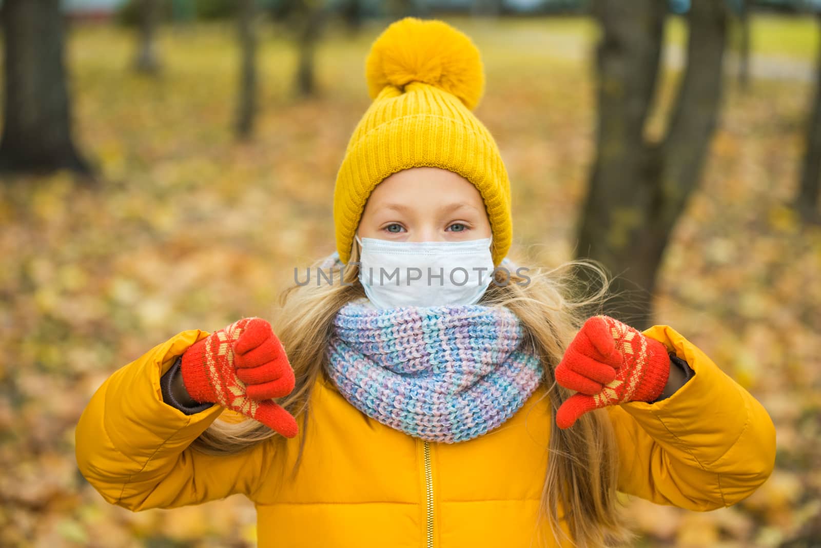 Little girl with blond hair wearing respirator mask in autumn background in yellow clothing