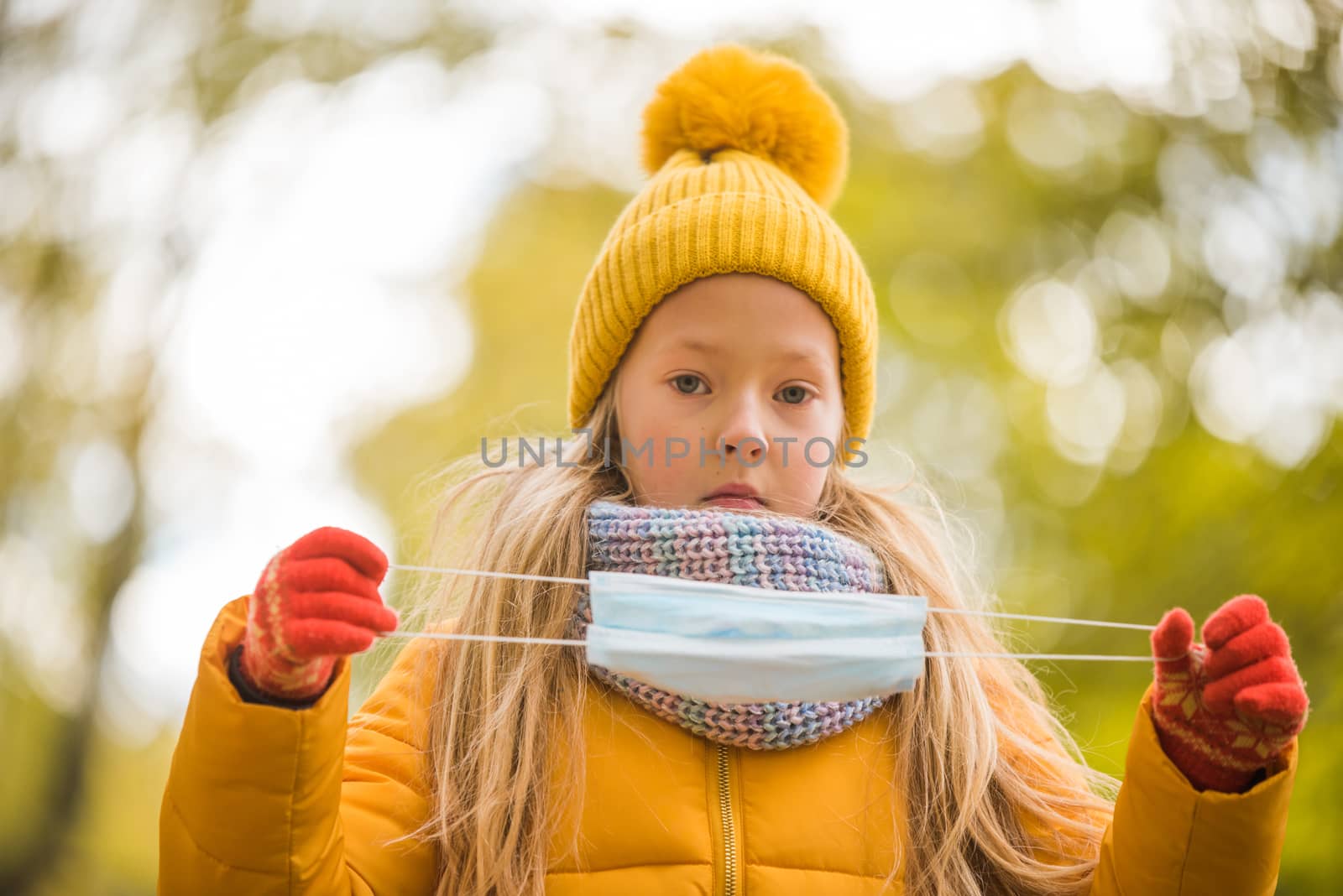 Little girl with blond hair wearing respirator mask in autumn background in yellow clothing