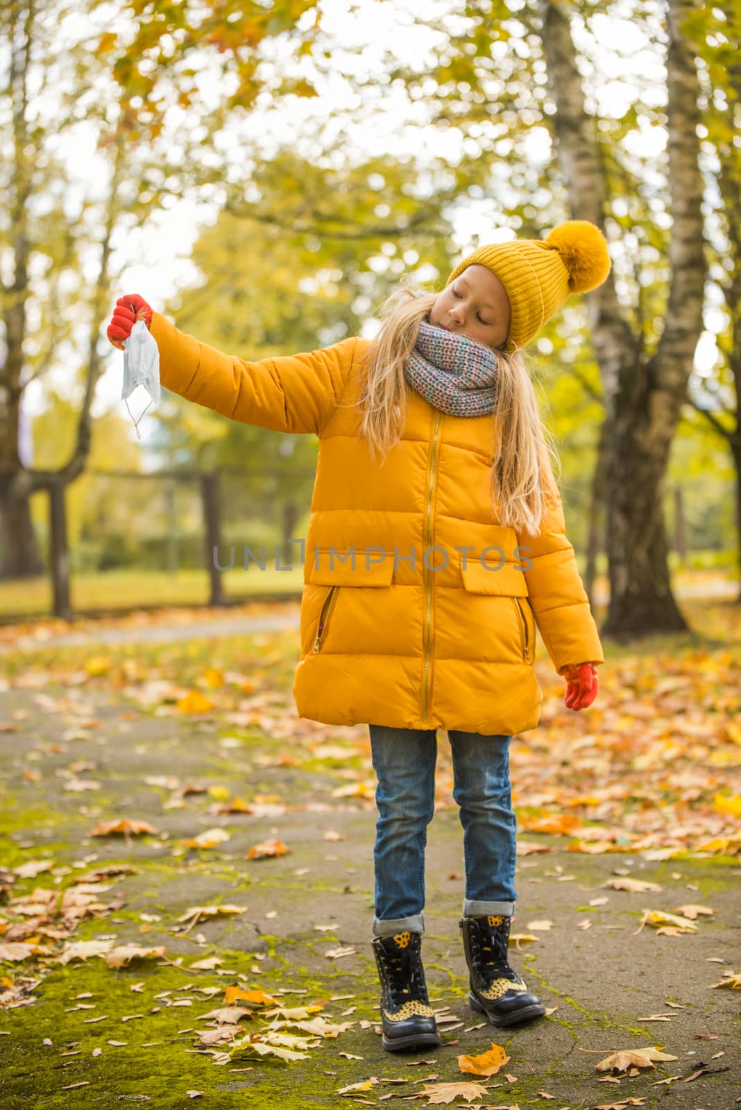 Little girl with blond hair wearing respirator mask in autumn background in yellow clothing