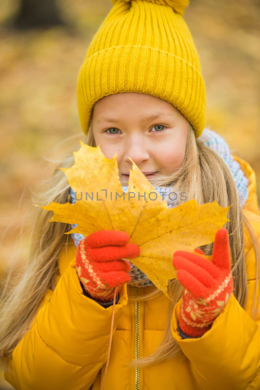 Little girl with blond hair in autumn background in yellow clothing with yellow leaf