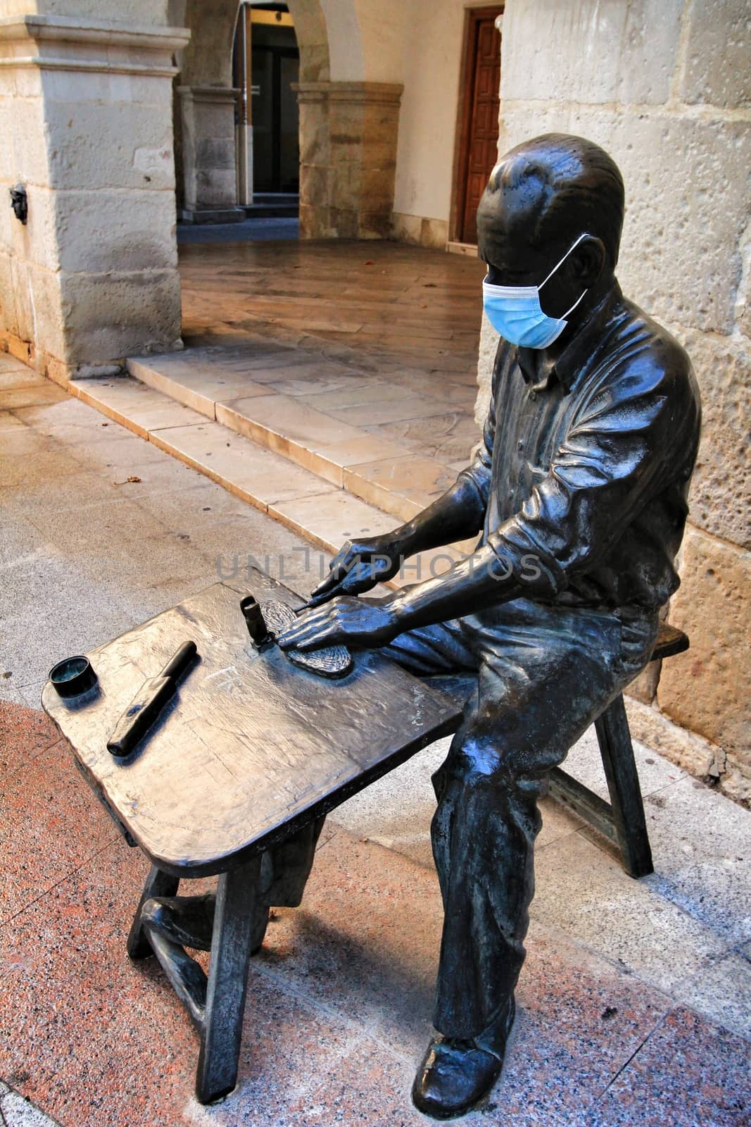 Elche, Alicante, Spain- September 9, 2020: Sculpture of a shoemaker worker covered with a mask in the main square of the Raval neighborhood in Elche
