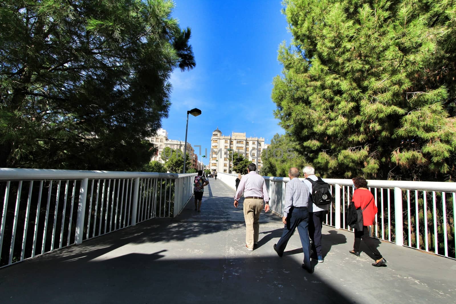 Elche, Alicante, Spain- October 7, 2020: People crossing a pedestrian bridge in the morning in Elche. Beautiful pine trees in both sides.
