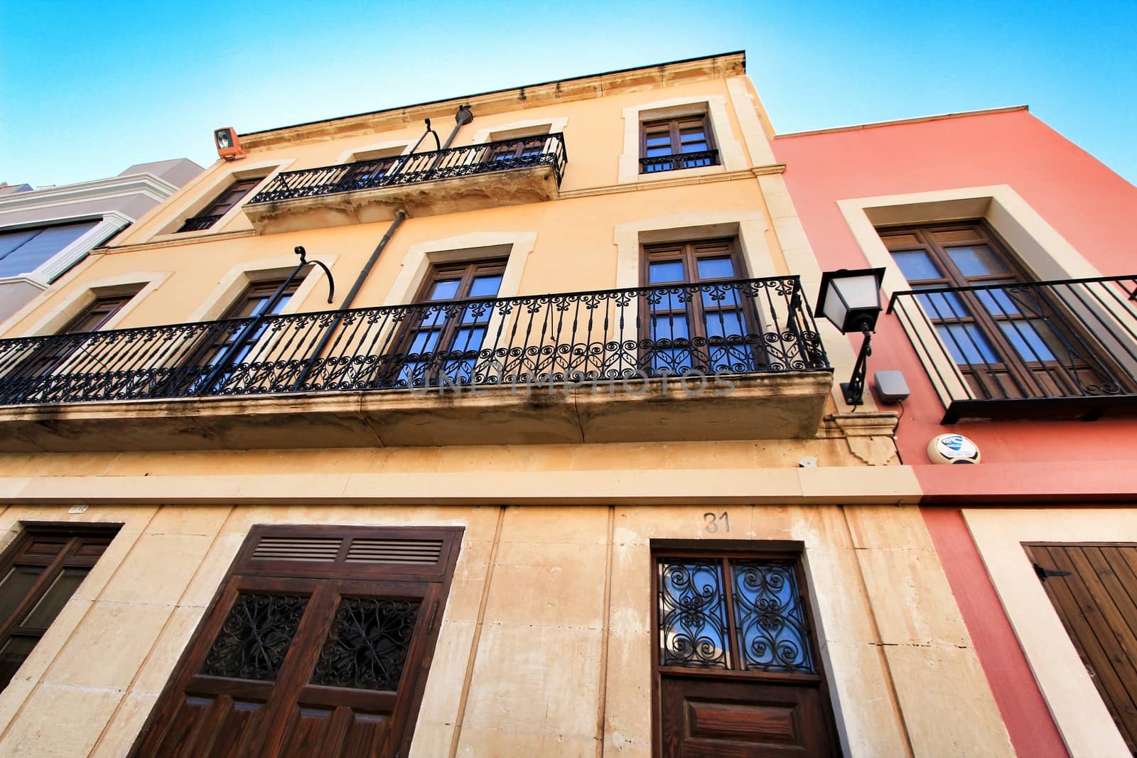 Elche, Alicante, Spain- September 9, 2020: Old colorful painted facades with vintage streetlight in Elche, Alicante, Spain. El Raval neighborhood.