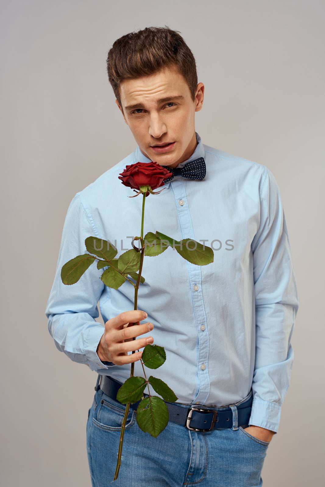 Romantic man with a red rose and in a blue shirt with a bow tie around his neck gray background by SHOTPRIME