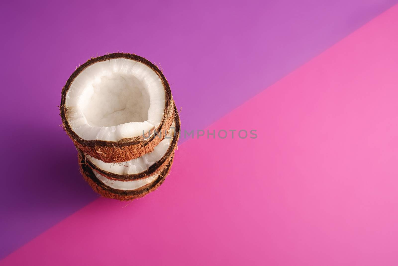 Stacked coconut fruits on violet and purple plain background, abstract food tropical concept, angle view copy space