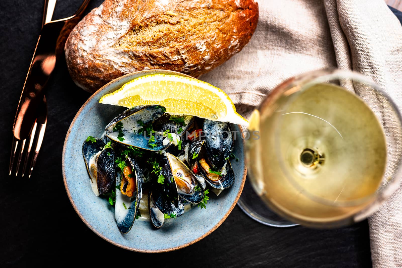 Cooked Blue mussels in clay dish with bread and white wine glass
