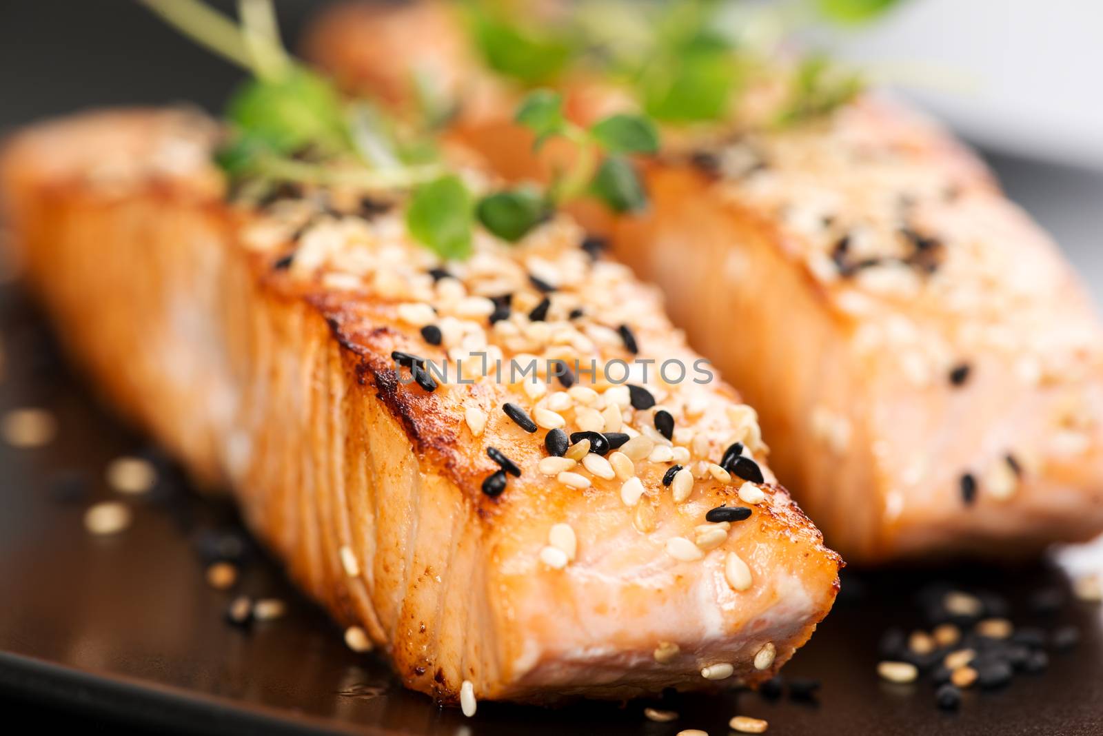 Grilled salmon, sesame seeds  and marjoram on a black plate. Studio shot