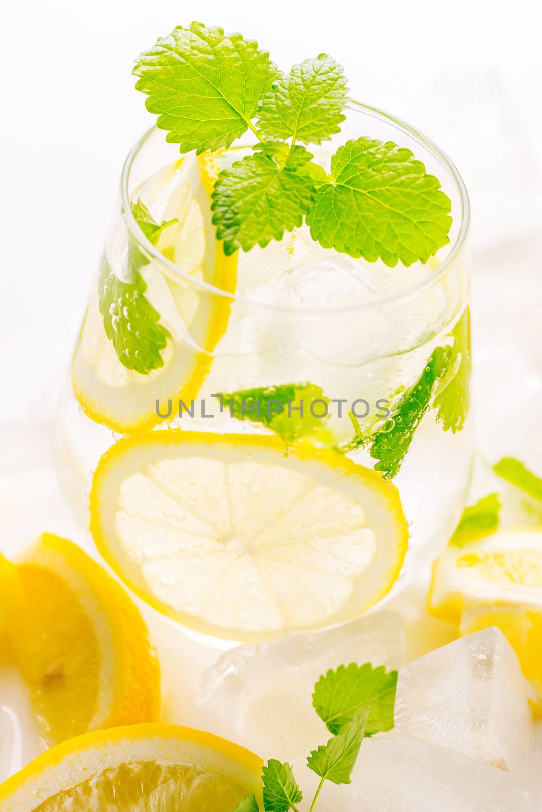 Lemonade drink in a glass: water, ice, lemon slice and mint on white background