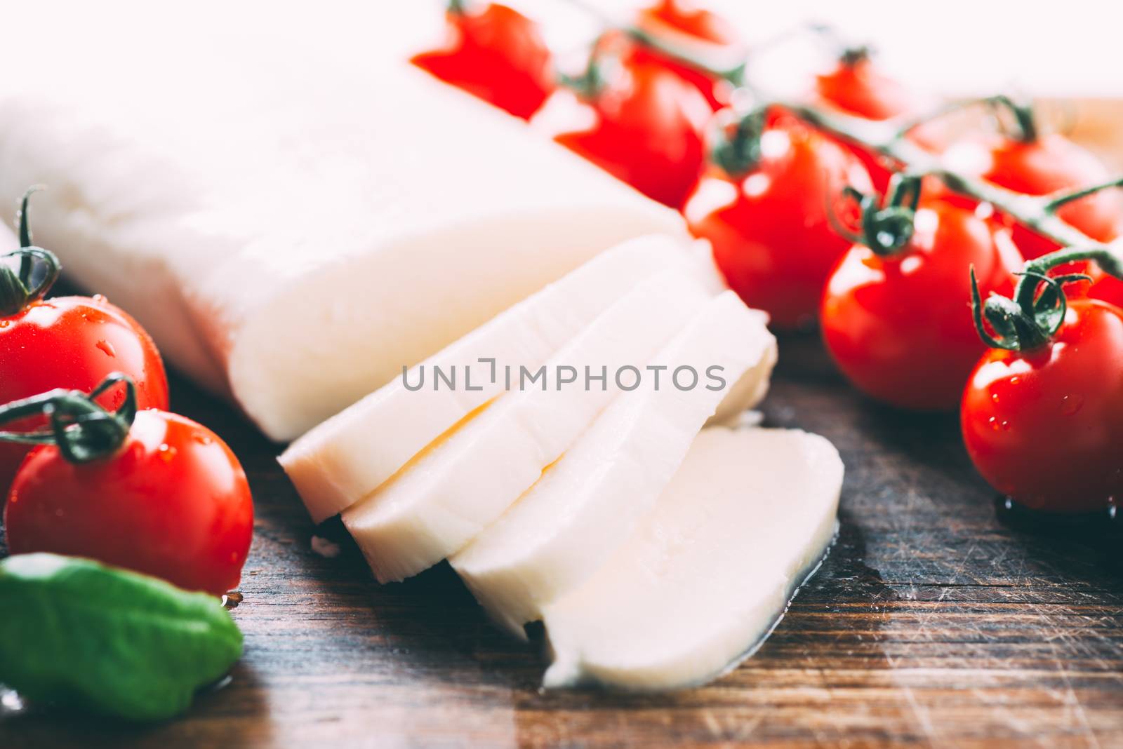 Mozzarella, cherry tomatoes and basil leaves on wooden cutting board by Nanisimova