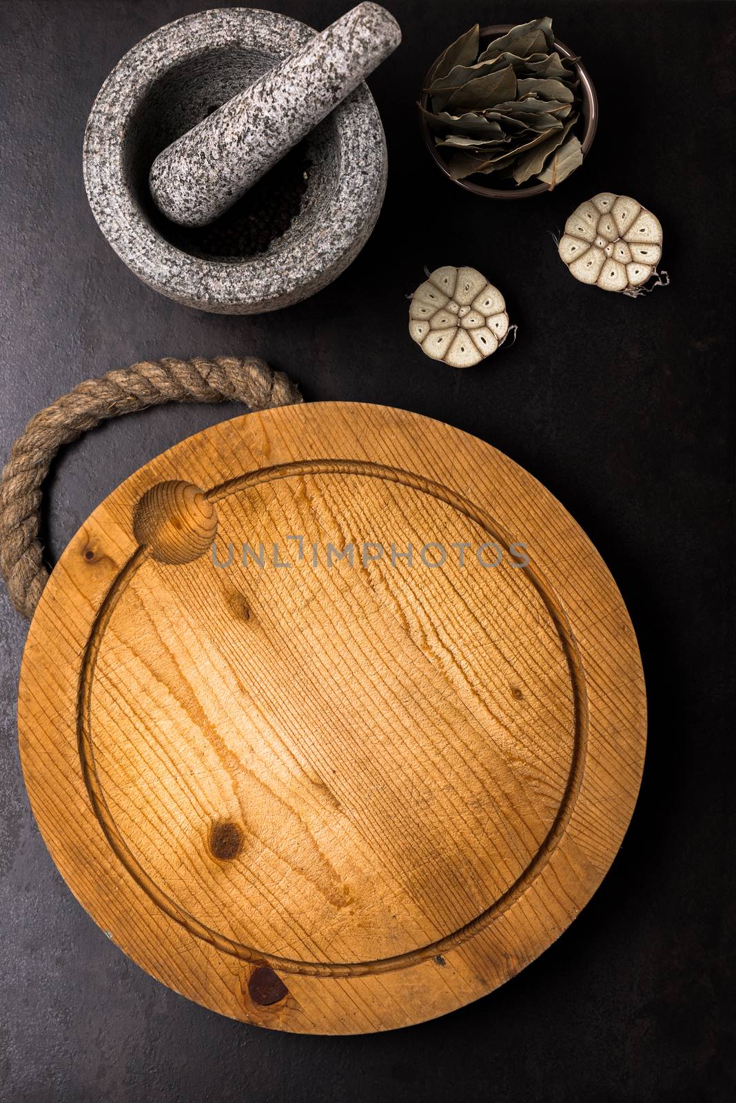 Stone mortar bowl with pestle garlic bay leaf and wooden cutting board by Nanisimova