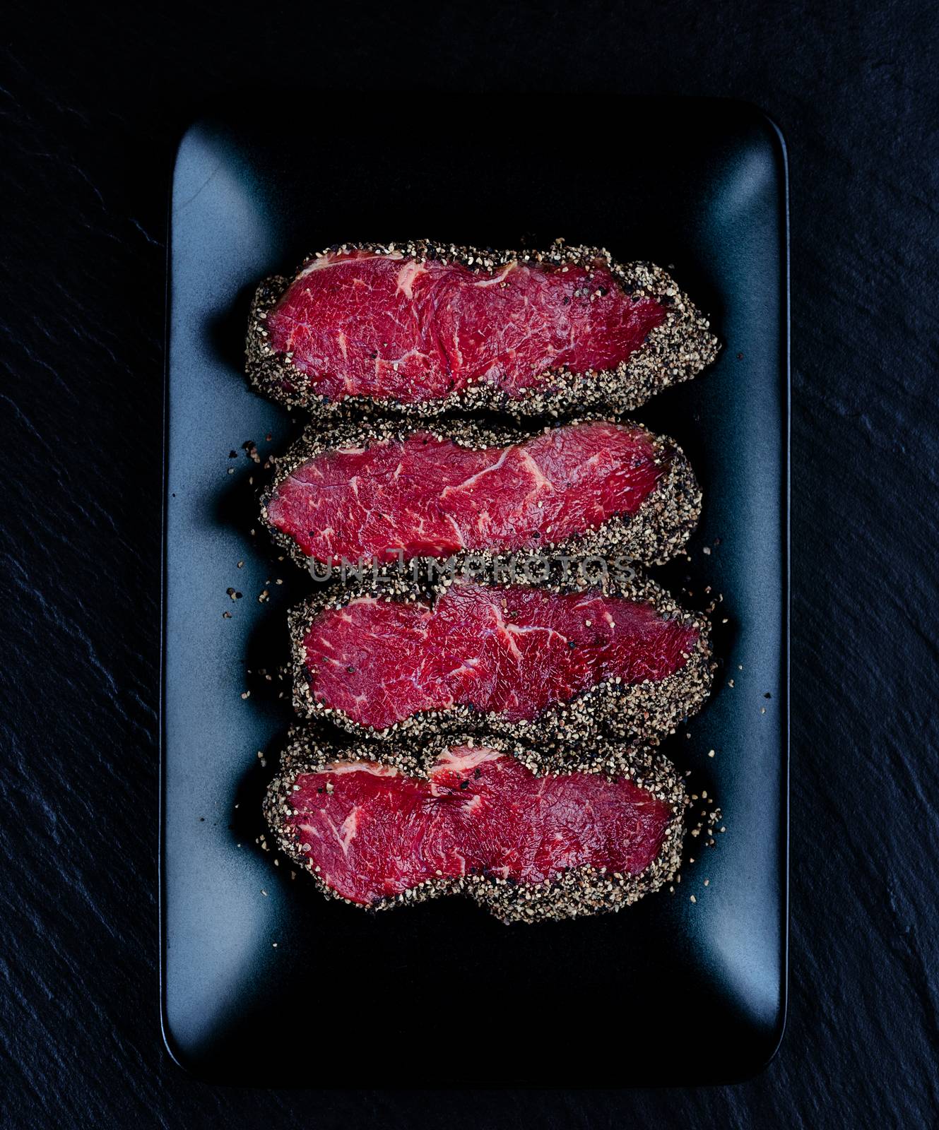 Pepper steaks on black stone plate top view
