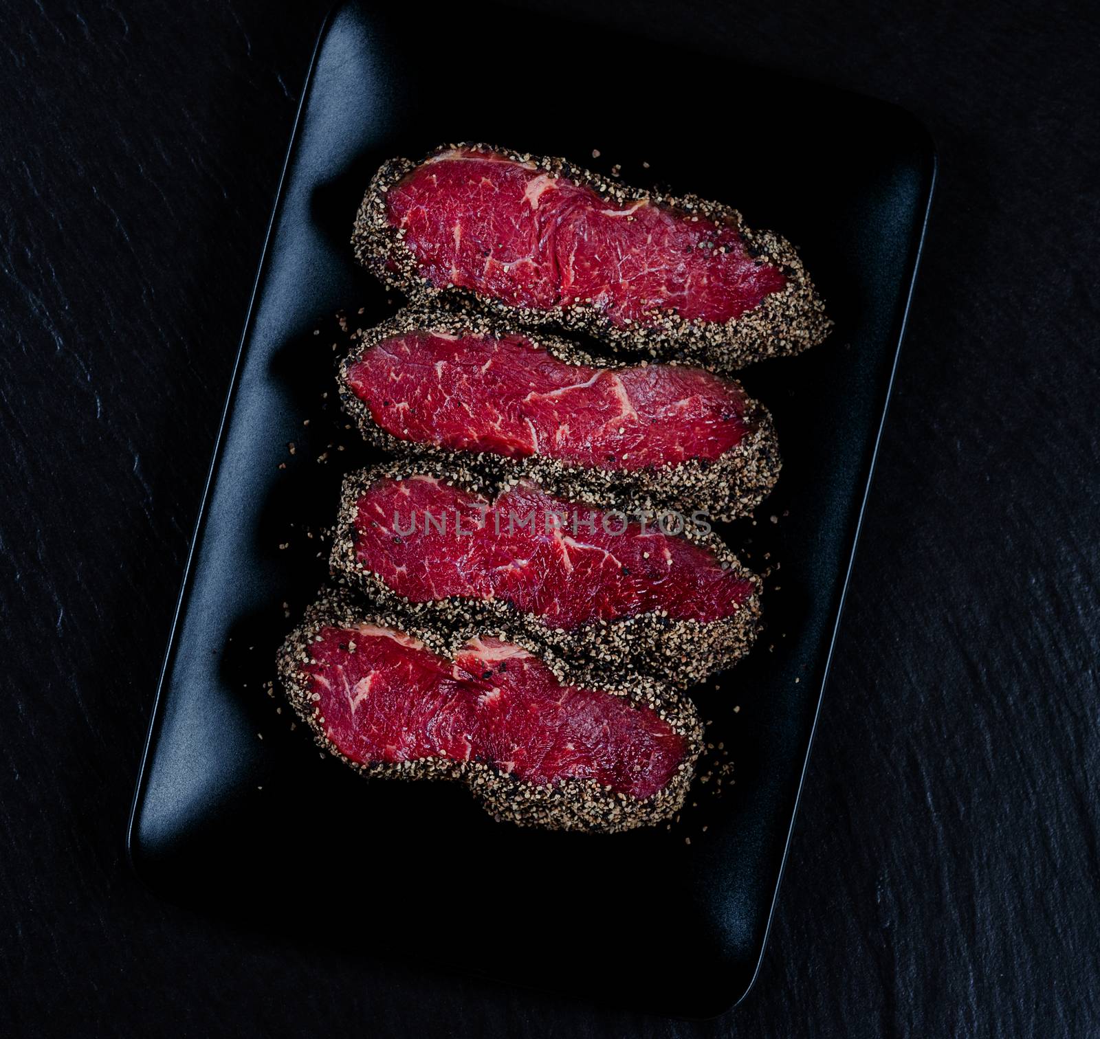 Top view on pepper steaks on black stone plate by Nanisimova