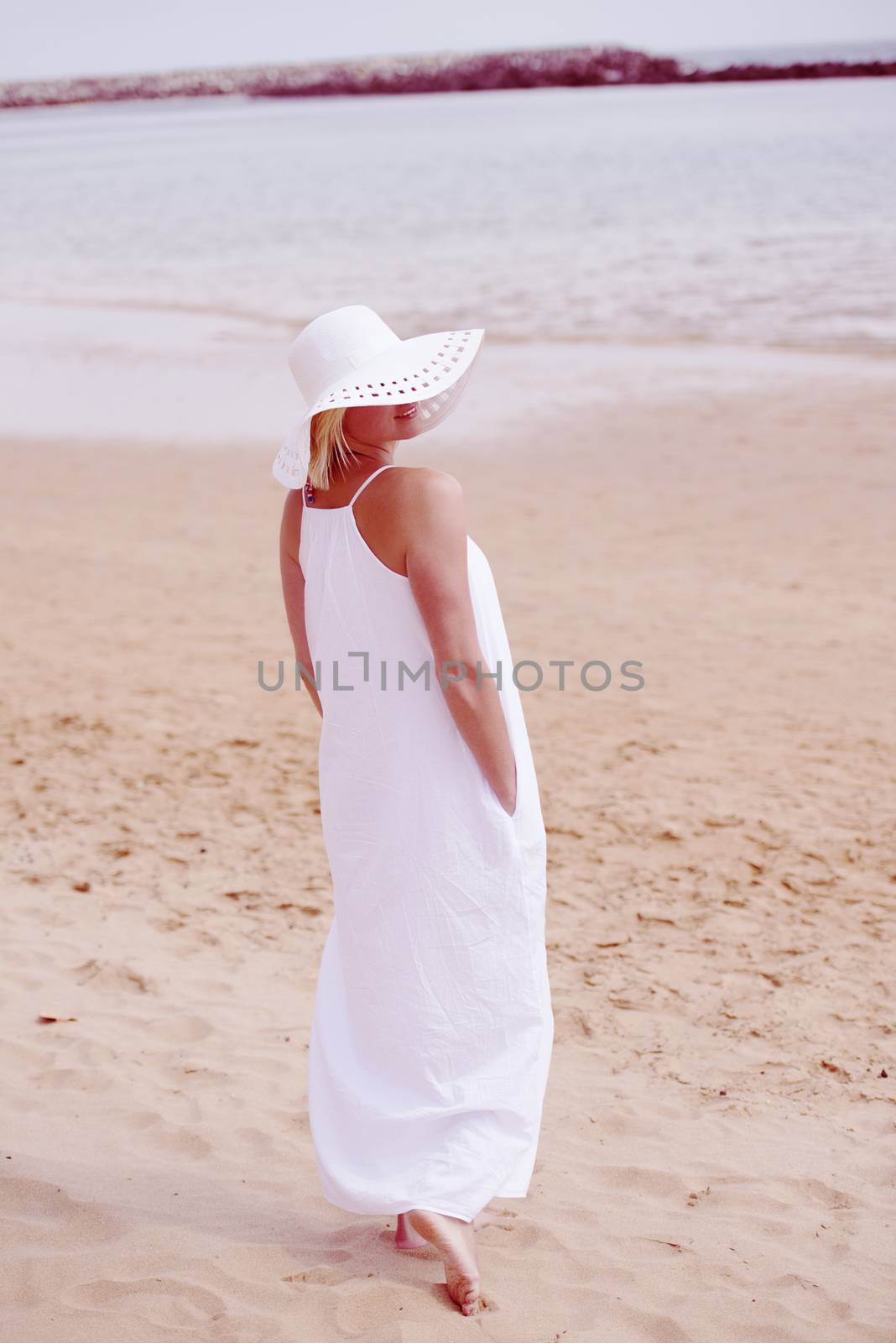 Woman walking on beach in long white dress and hat