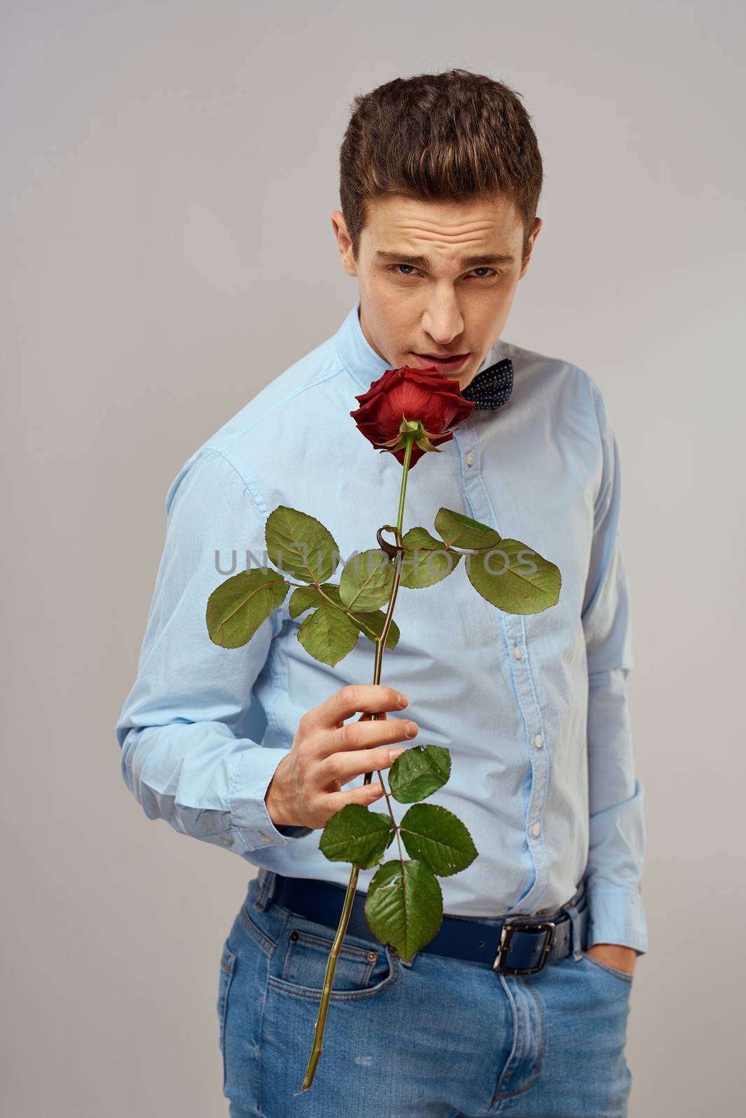 Romantic man with a red rose and in a blue shirt with a bow tie around his neck gray background. High quality photo