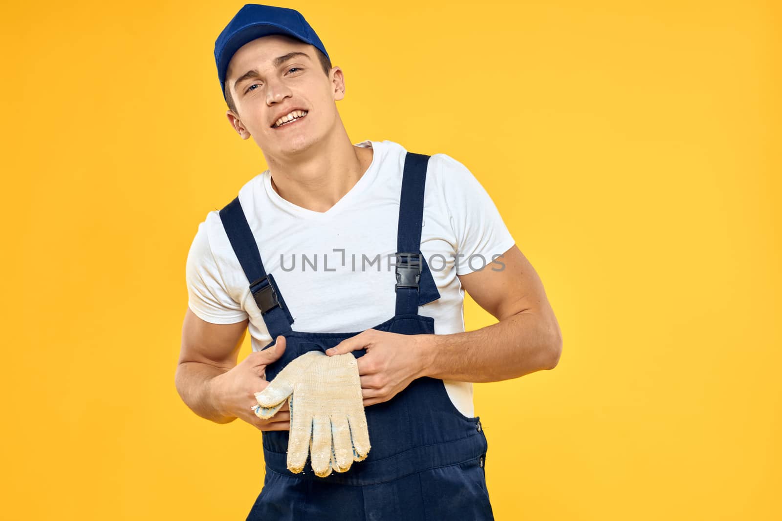 Working man in uniform of gloves rendering service yellow background by SHOTPRIME