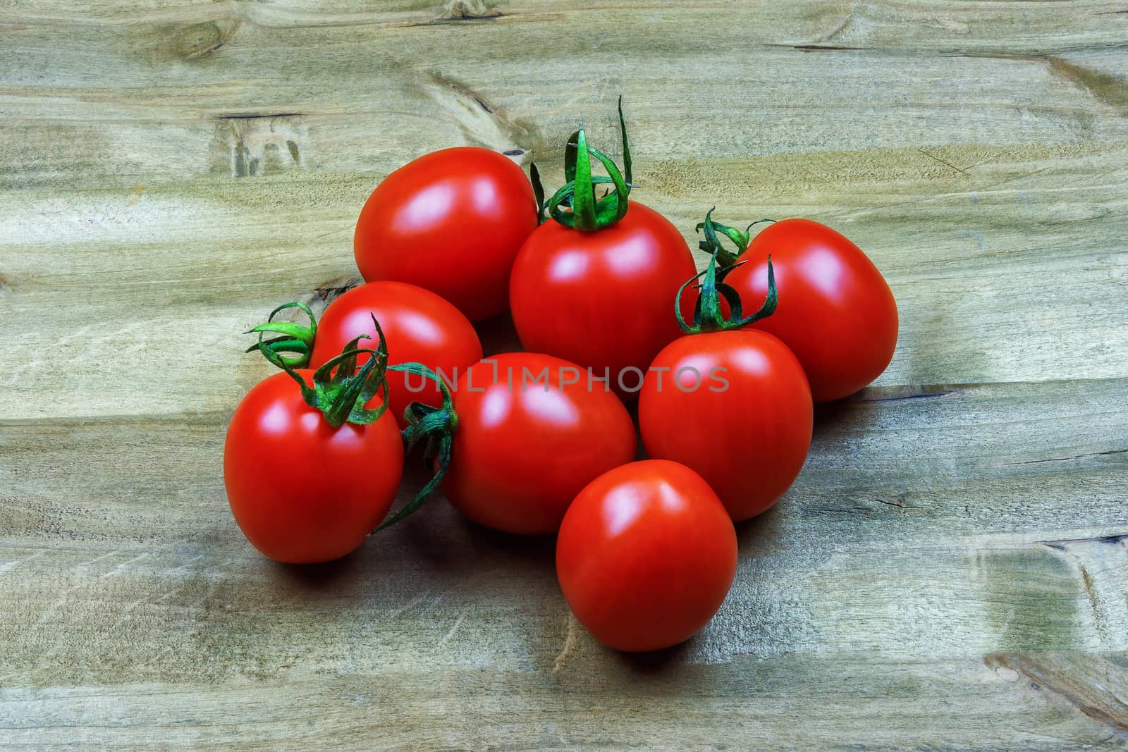 
Several small red tomatoes lie on a wooden surface