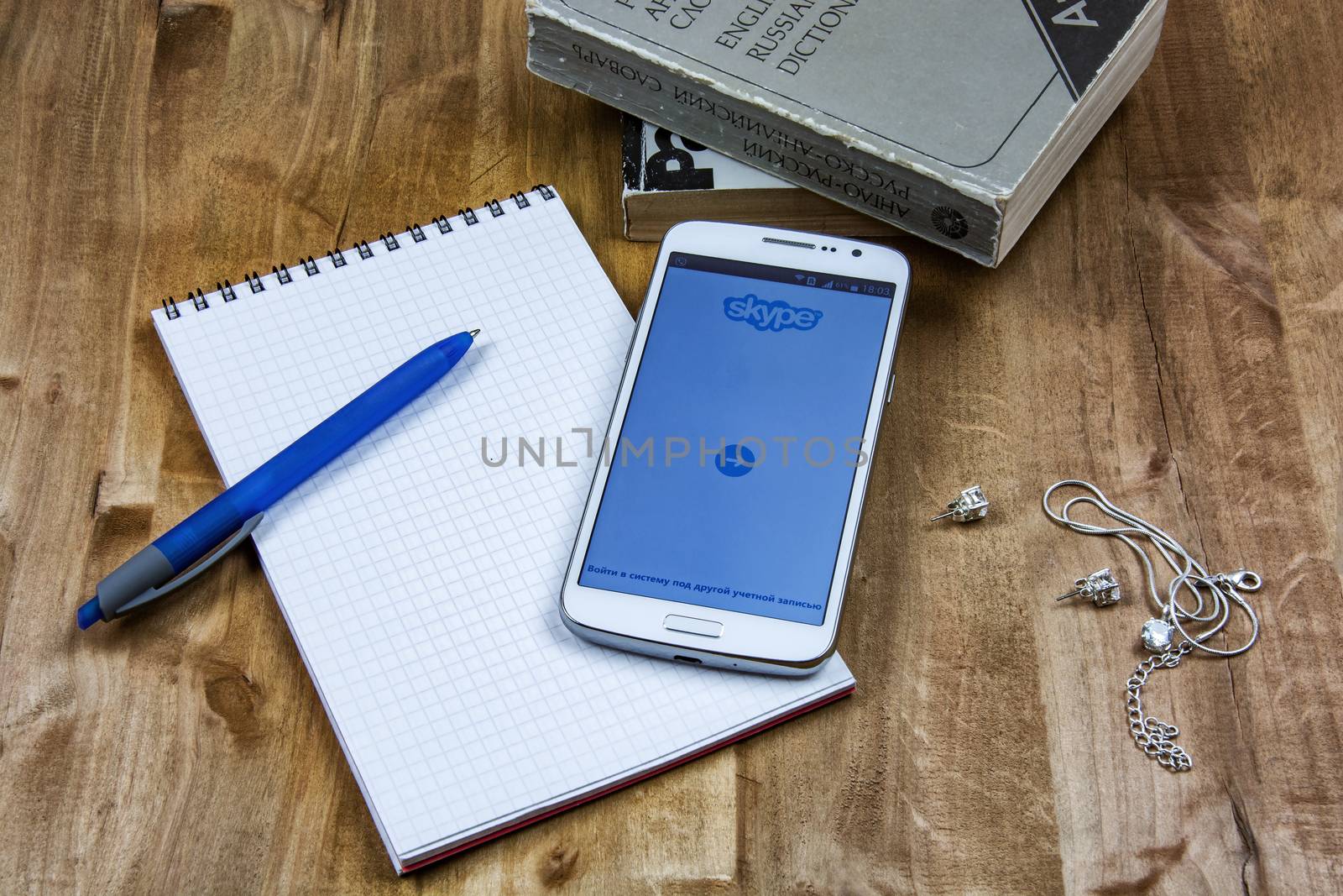 Books, notebook with pen and smartphone, chain and earrings lie on a wooden surface
