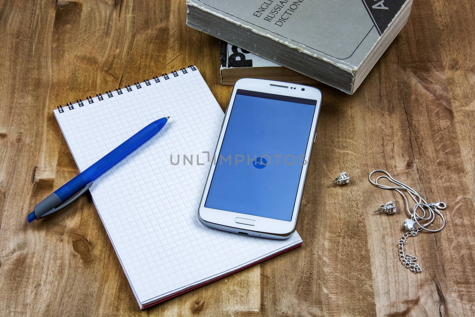 Books, notebook with pen and smartphone, chain and earrings lie on a wooden surface