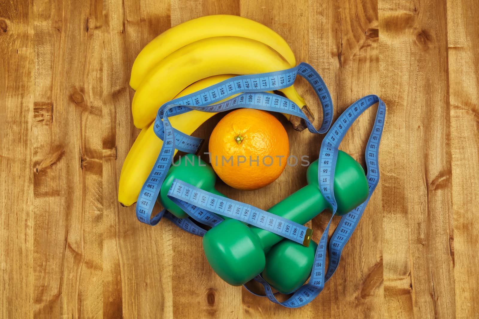 On the wooden surface are two dumbbells, centimeter, bananas and orange